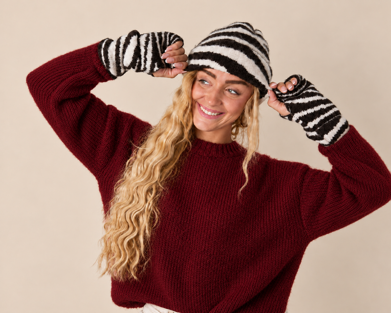 Vrouw met gestreepte muts en bijpassende handschoenen in een stijlvolle winterlook.