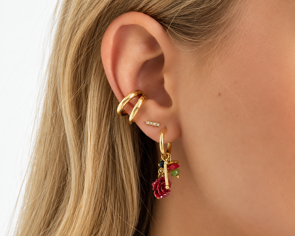 Model met goudkleurige ear cuffs en meerdere oorbellen, waaronder een hanger met kleurrijke details.