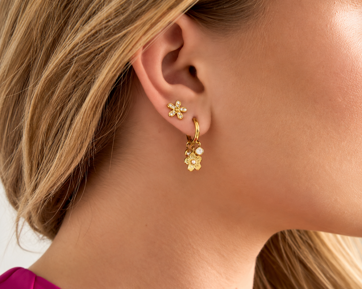 Model met goudkleurige oorbellen met bloemdetails en een tweede subtiele oorbel in het oor